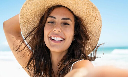 Picture of a young woman smiling and holding her beach hat